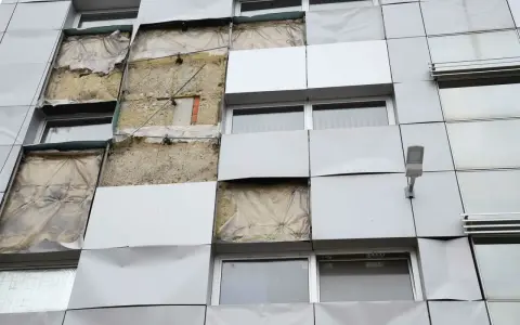 Facciata di un edificio con pannelli rimossi, mostrando l'isolamento. Si valuta la conducibilità termica dei materiali per l'efficienza energetica.