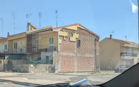 Edificio in fase di ristrutturazione, con facciata parzialmente scoperta che rivela la muratura. Sembra un condominio in attesa del suo nuovo cappotto.