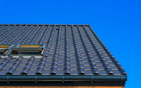 Coperture tetti moderni in tegole scure, con lucernari a vista sotto un cielo azzurro intenso.