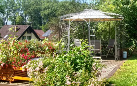 Un gazebo con un pavimento in legno fai da te, circondato da fiori colorati e vegetazione lussureggiante.