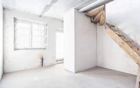 Interno grezzo con finestra, porta finestra e scala in legno grezzo. Ambiente in fase di ristrutturazione, un futuro piano seminterrato.