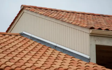 Tegole rosse su un tetto, con pannelli verticali beige e una grondaia. Le scossaline proteggono il bordo del tetto.