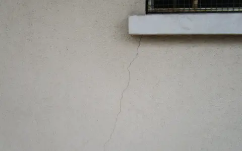 Crepa sottile su muro esterno, vicino a davanzale e inferriata. Necessaria riparazione crepe strutturali.