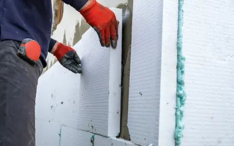 Operaio posa pannelli isolanti per cappotto termico, attenzione alle fughe e alle soglie per evitare ponti termici.