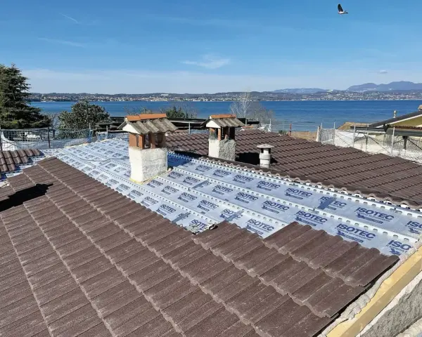 Tegole tetto moderne marroni in fase di posa su un tetto con vista lago. Sotto le tegole, una membrana isolante.