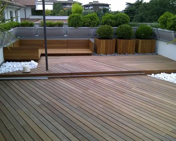 Un balcone trasformato con un pavimento in legno fai da te, circondato da piante e arredi moderni.