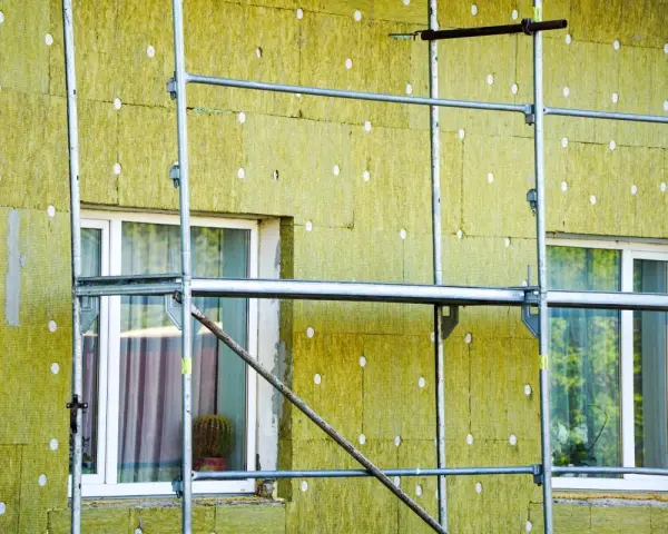 Installazione di un cappotto termico su un edificio, con ponteggi metallici che circondano la facciata isolata. La durata del cappotto termico è garantita da materiali di qualità.