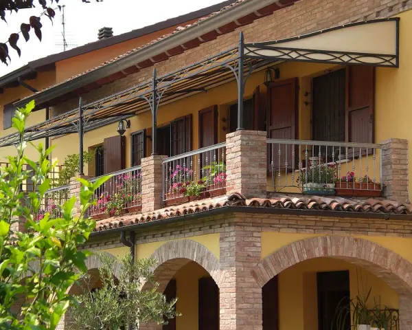 Il montaggio scossalina balcone protegge la facciata. Balcone fiorito con ringhiera in ferro battuto e tettoia decorata.