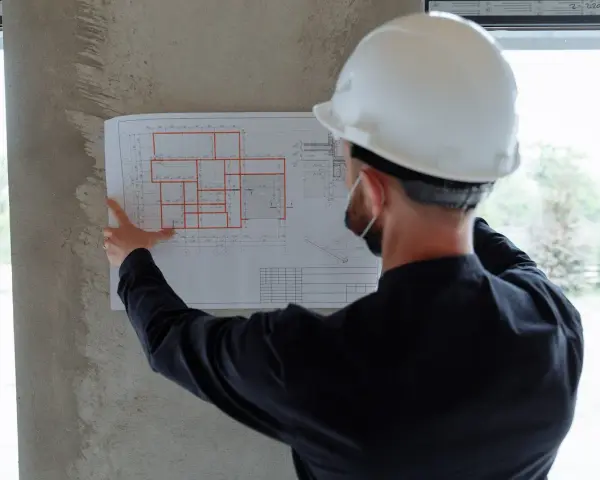 Un ingegnere con casco bianco esamina un progetto, segno che i migliori general contractor pianificano ogni dettaglio.