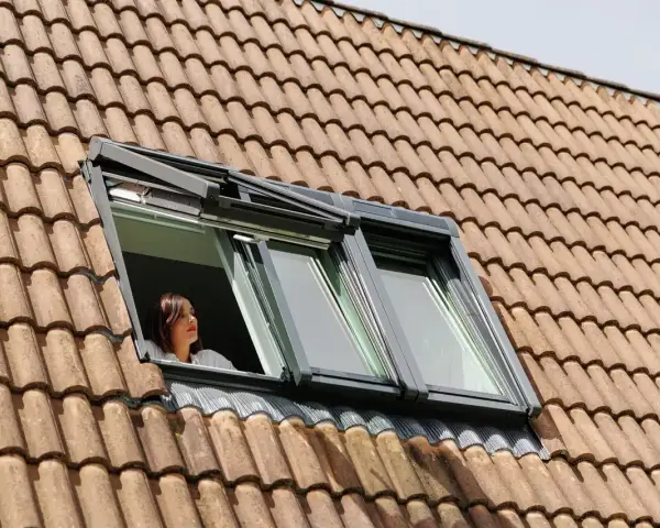 Donna guarda fuori da una finestra sul tetto, un esempio di come isolare il tetto dall'esterno per un maggiore comfort.