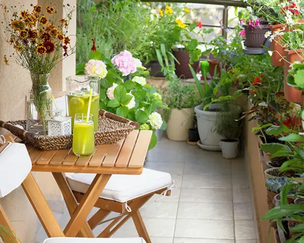 Un terrazzo fiorito e accogliente, perfetto per chi cerca idee su come abbellire un terrazzo fai da te. Tavolino in legno con bevanda rinfrescante e fiori colorati.