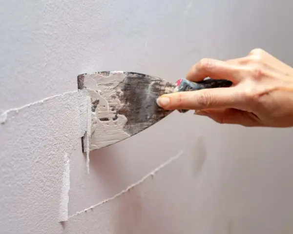 Mano usa una spatola per rimuovere la vecchia pittura, mostrando come grattare un muro per prepararlo.