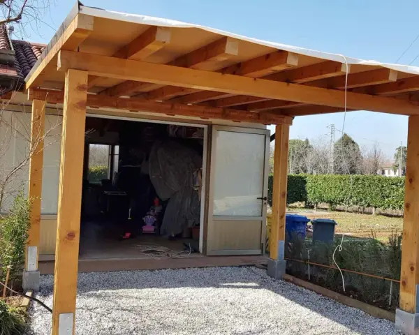 Una tettoia fai da te in legno protegge un'entrata, con un tetto in telo bianco e pilastri robusti.