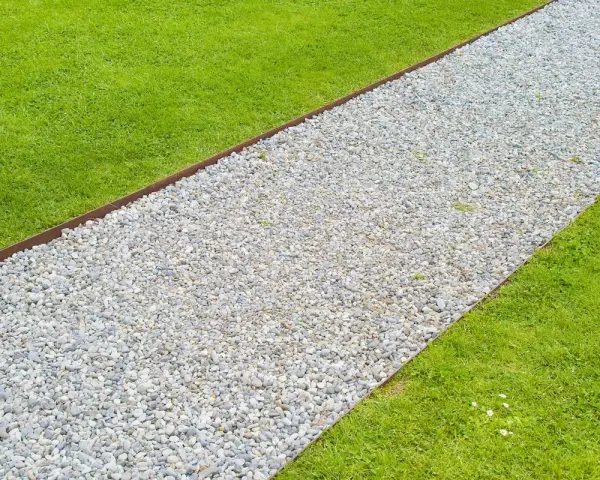 Un percorso di ghiaia bianca delimita un prato verde brillante, creando un vialetto giardino invitante.