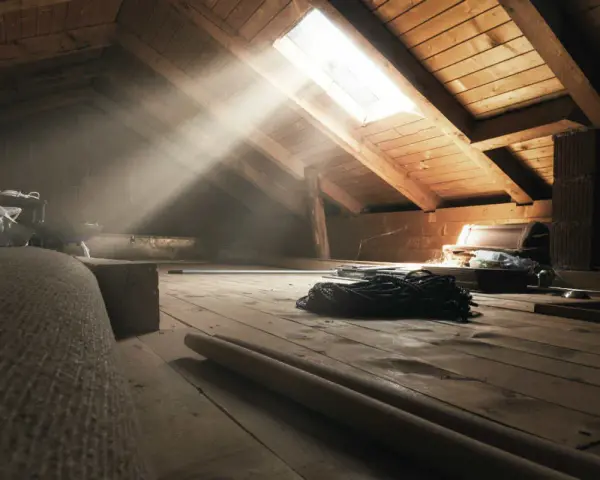Raggi di sole illuminano un sottotetto non abitabile, pieno di oggetti dimenticati e travi di legno.
