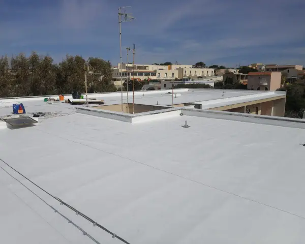Tetto piano bianco appena impermeabilizzato senza rifarlo, con antenne e edifici sullo sfondo.