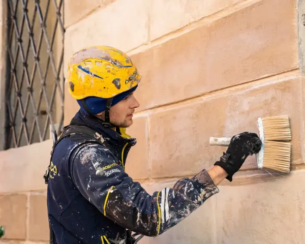 Operaio con casco giallo applica soluzione per pulire muro esterno con candeggina.