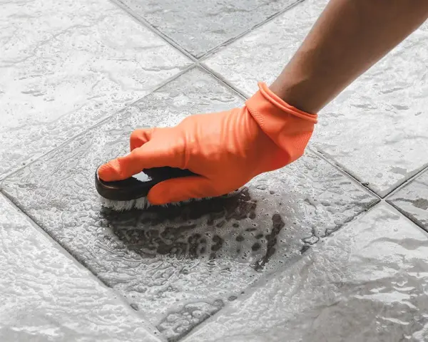 Mano con guanto arancione che strofina il pavimento del terrazzo con una spazzola, per togliere la ruggine e lo sporco.