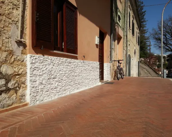 Una parete umida è stata rivestita con pietre bianche, migliorando l'estetica e la protezione dell'edificio.