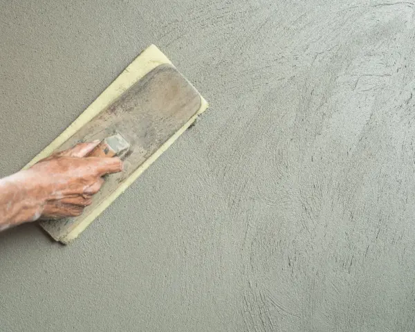 Mano che stende l'intonaco con una spatola. Dopo l'intonaco posso pitturare la parete.
