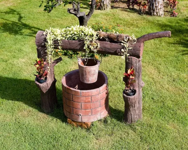 Pozzo decorativo in mattoni con secchio appeso, circondato da verde. Un'idea per capire quanto costa fare un pozzo.