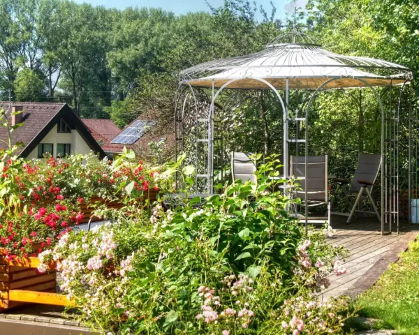 Un gazebo con un pavimento in legno fai da te, circondato da fiori colorati e vegetazione lussureggiante.