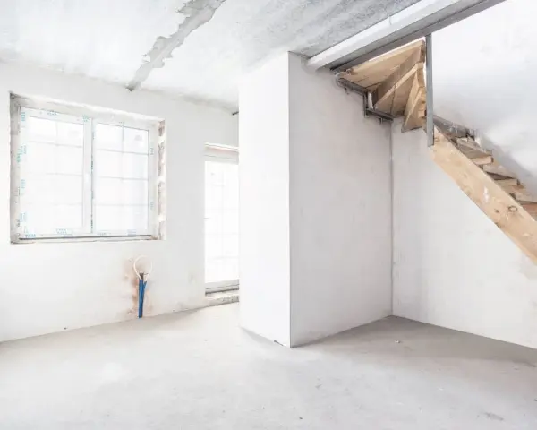 Interno grezzo con finestra, porta finestra e scala in legno grezzo. Ambiente in fase di ristrutturazione, un futuro piano seminterrato.