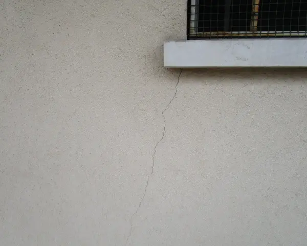 Crepa sottile su muro esterno, vicino a davanzale e inferriata. Necessaria riparazione crepe strutturali.