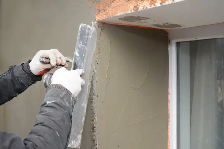 Lavori di intonacatura attorno alle spallette delle finestre, con un operaio che stende il materiale.