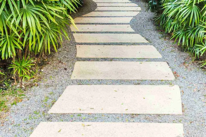 Un sentiero sinuoso con lastre di pietra e ghiaia, circondato da vegetazione lussureggiante. Idee marciapiede casa per un ingresso accogliente.