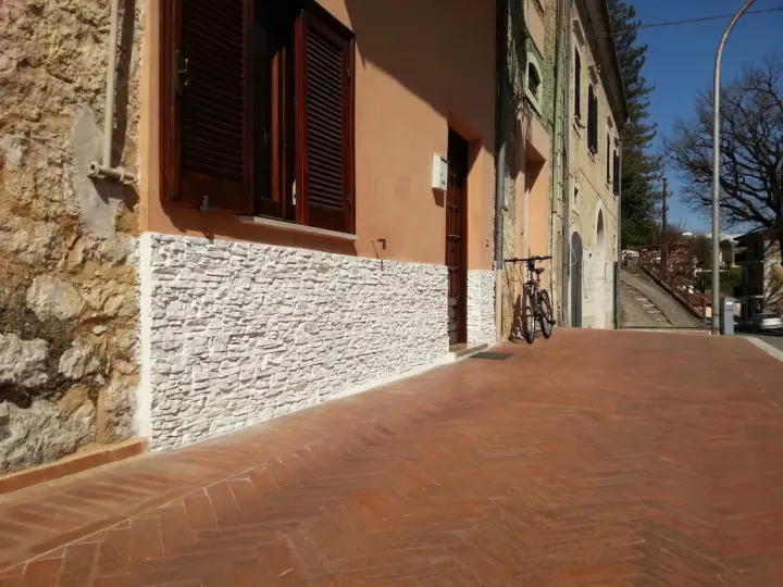 Una parete umida è stata rivestita con pietre bianche, migliorando l'estetica e la protezione dell'edificio.