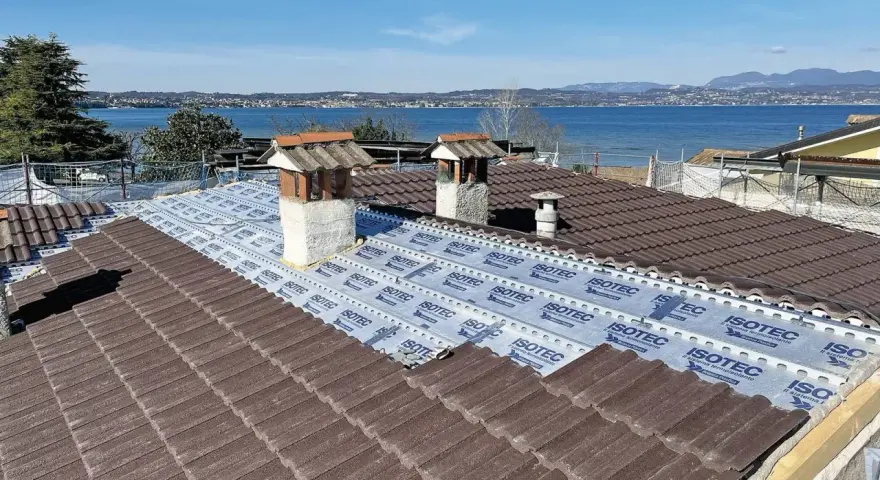 Tegole tetto moderne marroni in fase di posa su un tetto con vista lago. Sotto le tegole, una membrana isolante.