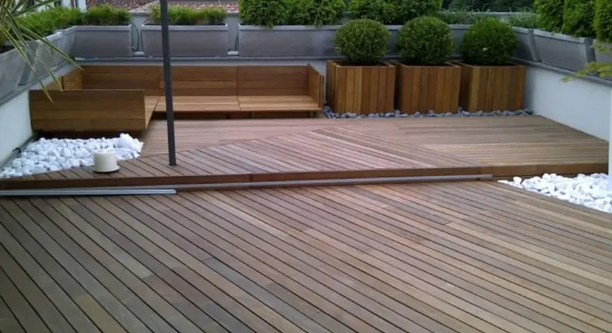 Un balcone trasformato con un pavimento in legno fai da te, circondato da piante e arredi moderni.