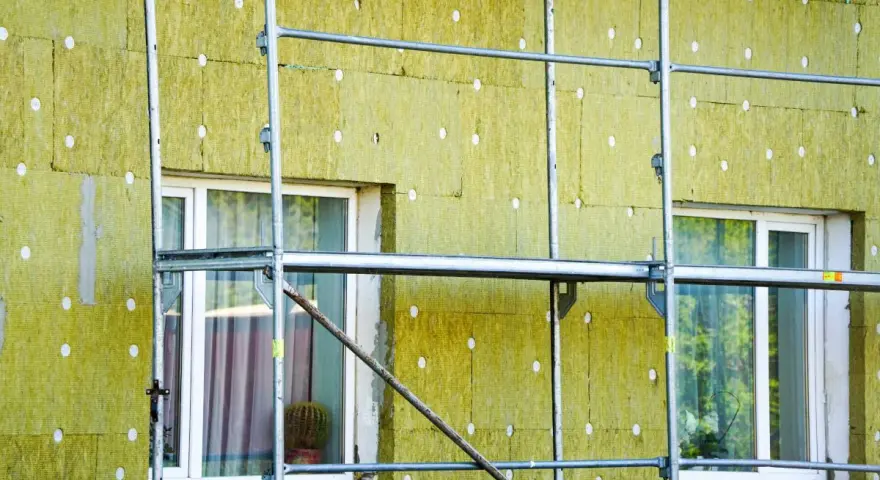 Installazione di un cappotto termico su un edificio, con ponteggi metallici che circondano la facciata isolata. La durata del cappotto termico è garantita da materiali di qualità.