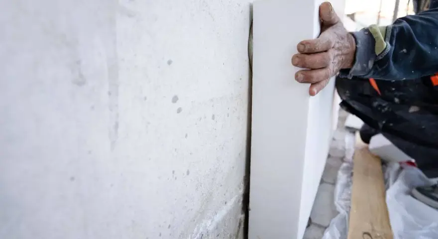 Mano di un operaio posiziona pannelli sottovuoto per isolare una parete grezza.