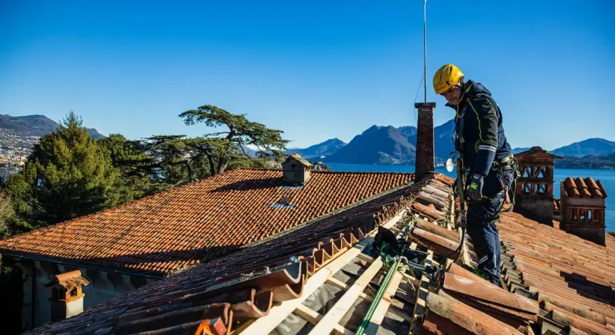 Operaio con imbracatura lavora alla costruzione tetti in legno, con vista su lago e montagne.