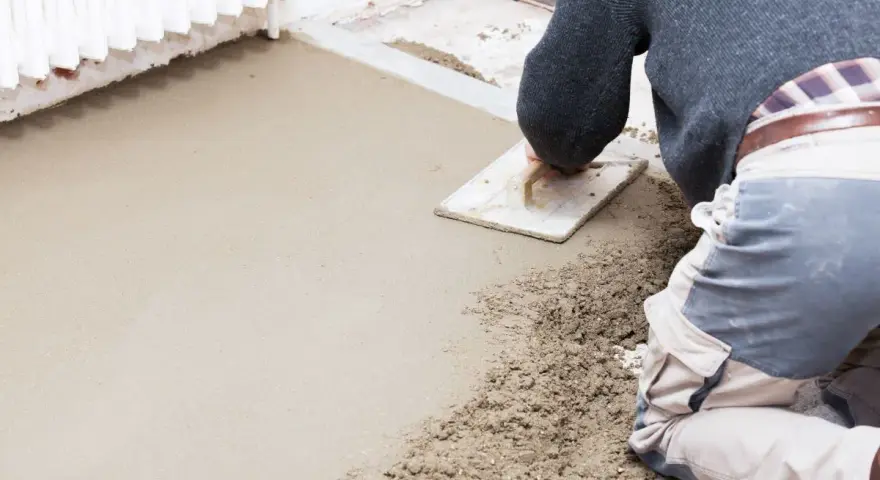 Operaio al lavoro con una cazzuola, livella il cemento per aumentare l'altezza del pavimento.