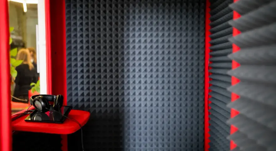 Cabina insonorizzata con pannelli fonoassorbenti, cuffie e tablet. Ideale per registrazioni audio.