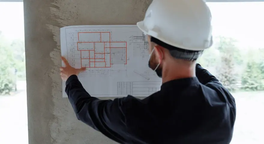 Un ingegnere con casco bianco esamina un progetto, segno che i migliori general contractor pianificano ogni dettaglio.
