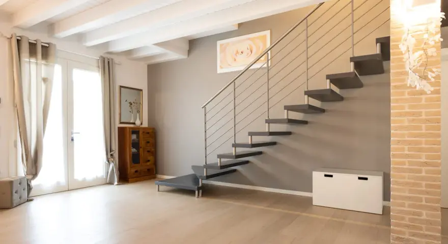 Moderna scala a sbalzo, soluzione per chi ha una scala troppo ripida. Arredamento minimalista con mobili in legno e tessuti chiari.