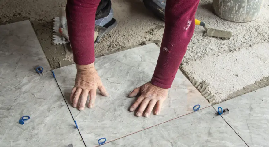 Mani esperte posano mattonelle con precisione, usando livellatori per un risultato perfetto.