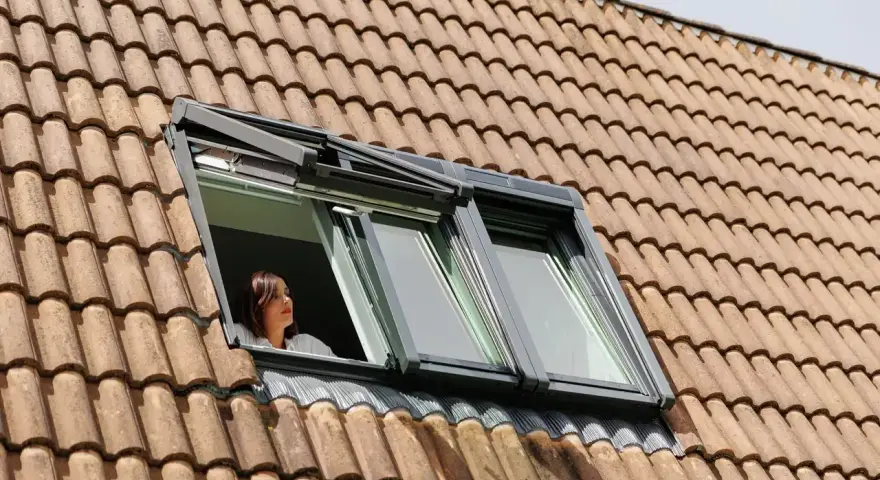 Donna guarda fuori da una finestra sul tetto, un esempio di come isolare il tetto dall'esterno per un maggiore comfort.