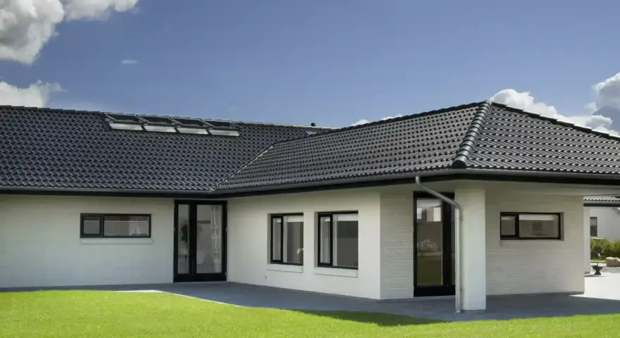 Casa moderna con tetto a padiglione scuro, finestre a tetto e prato verde.