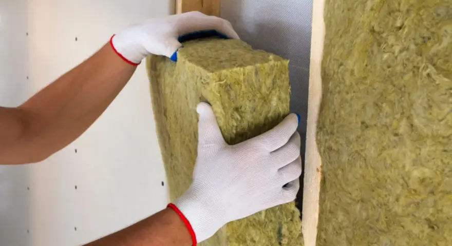 Mani guantate posizionano un pannello isolante, creando un cappotto interno o esterno per una parete.