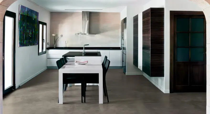 Modern kitchen with a dining area. The **pavimento in cemento per interni costi** is visible, offering a sleek and contemporary look.