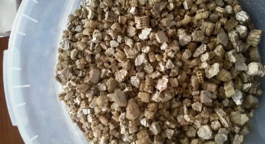 Granuli di vermiculite espansa isolante termico in un secchio bianco. Materiale leggero e poroso, ideale per l'edilizia.