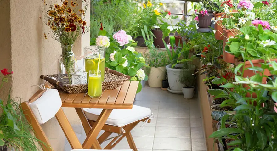 Un terrazzo fiorito e accogliente, perfetto per chi cerca idee su come abbellire un terrazzo fai da te. Tavolino in legno con bevanda rinfrescante e fiori colorati.