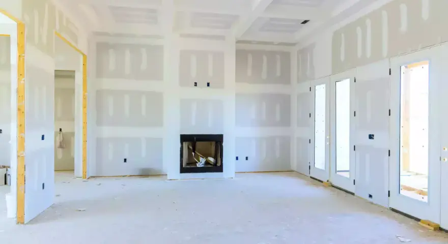 Interno di una casa in costruzione con pareti e soffitto in cartongesso, camino e porte a doppio battente.