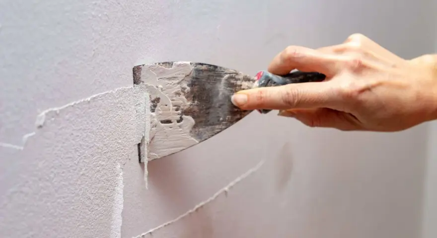 Mano usa una spatola per rimuovere la vecchia pittura, mostrando come grattare un muro per prepararlo.