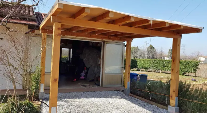 Una tettoia fai da te in legno protegge un'entrata, con un tetto in telo bianco e pilastri robusti.